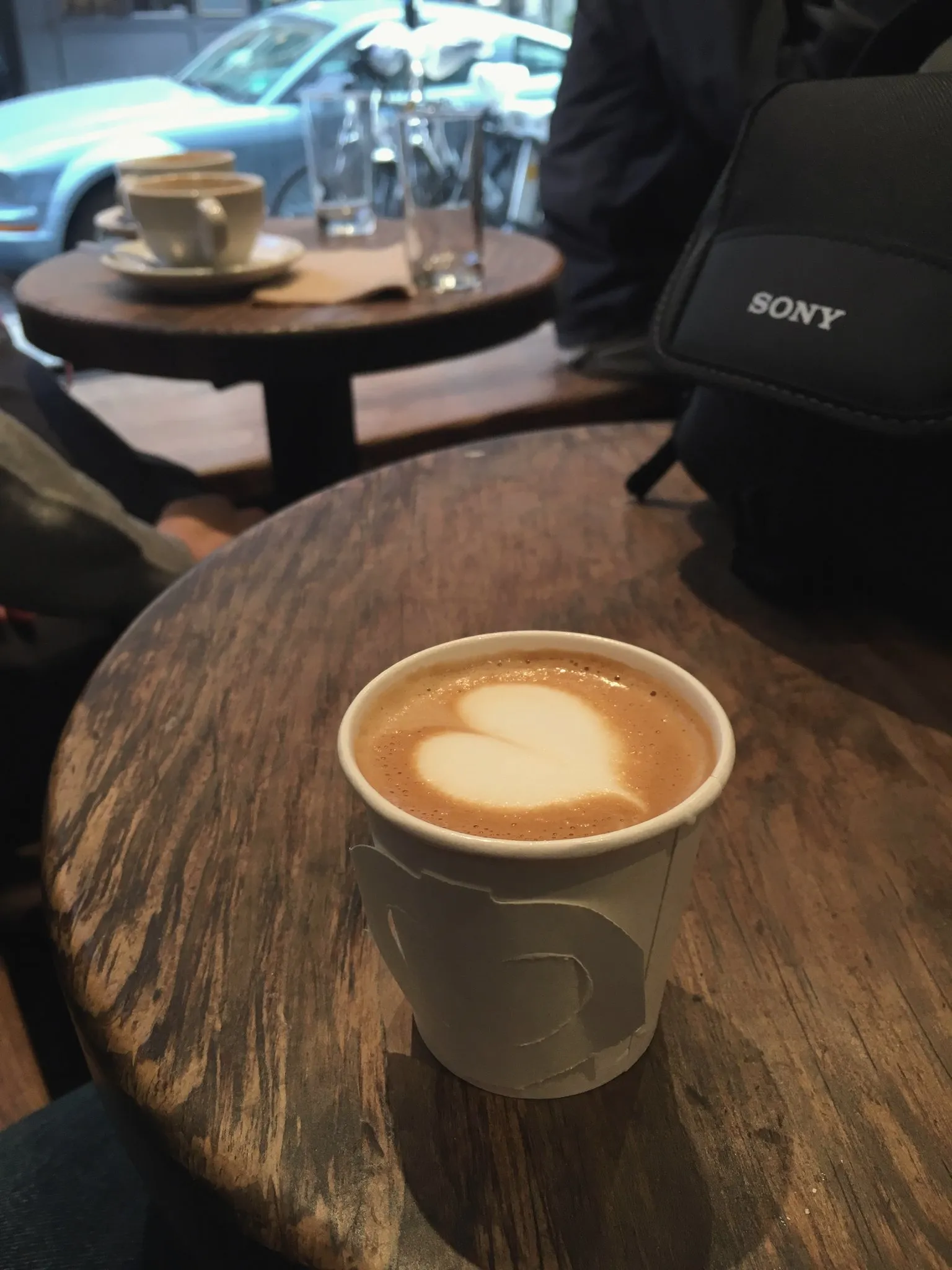 A flat white with latte art on a round wooden stump table