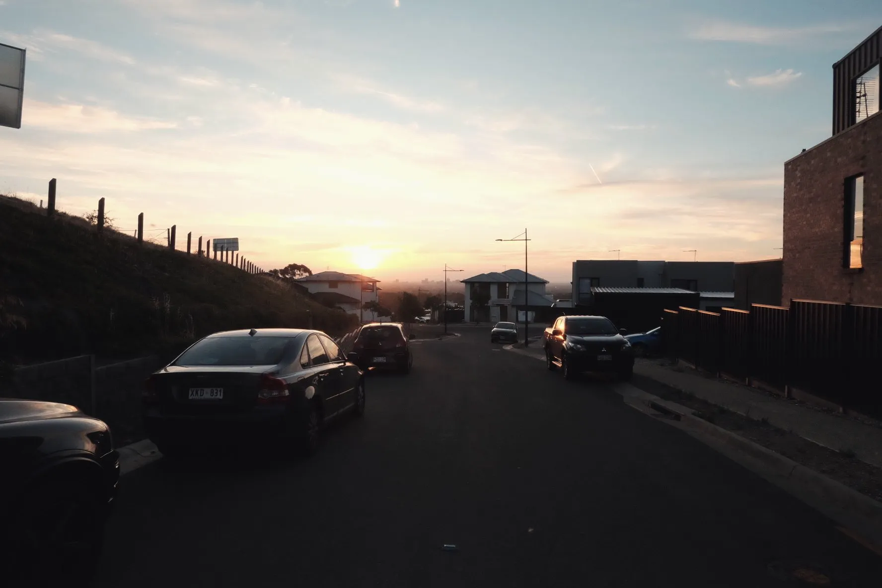 A suburban street with parked cars under a sunset sky